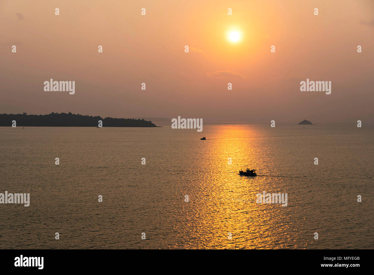 the sun falls in the sea near Singapore and the fishing boats continue their work Stock Photo