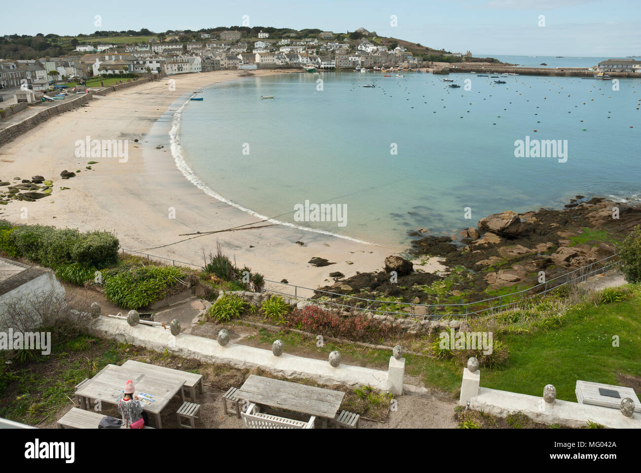 High view point showing Town Beach, St Mary's Harbour and Hugh Town on a sunny Spring morning, with pale blue calm sea and sky. Stock Photo