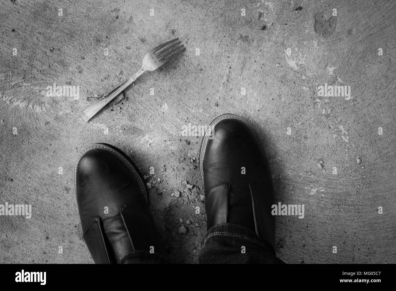 A black and white image of a fork lying on the ground near a person's feet Stock Photo