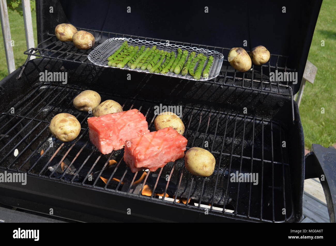 Watermelon, potatoes, and asparagus cooking on the outdoor backyard BBQ grill on a summer Sunday afternoon. Stock Photo