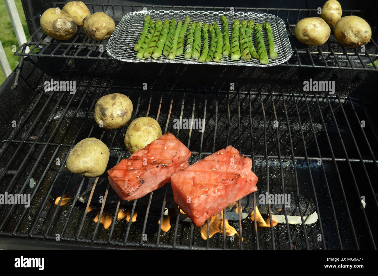 Watermelon, potatoes, and asparagus cooking on the outdoor backyard BBQ grill on a summer Sunday afternoon. Stock Photo