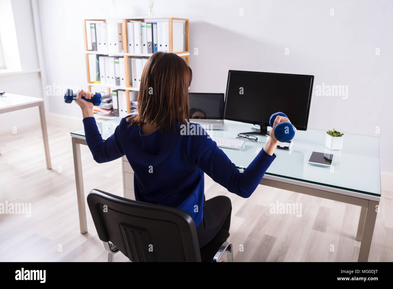 Young Businesswoman Sitting On Chair Doing Workout With Dumbbell Stock Photo