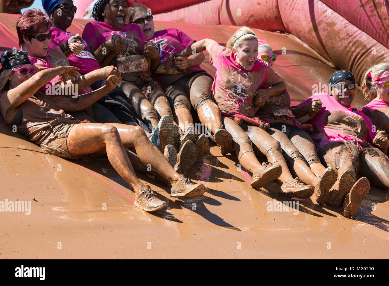 A group of muddy women holds hands as they slide down toward a mud pit at the Dirty Girl Mud Run obstacle course on April 23, 2016 in Hampton, GA. Stock Photo