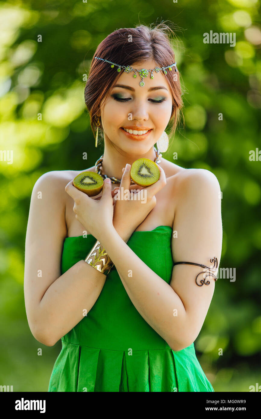 Portrait of a beautiful young asian woman holding two halves of kiwi ...