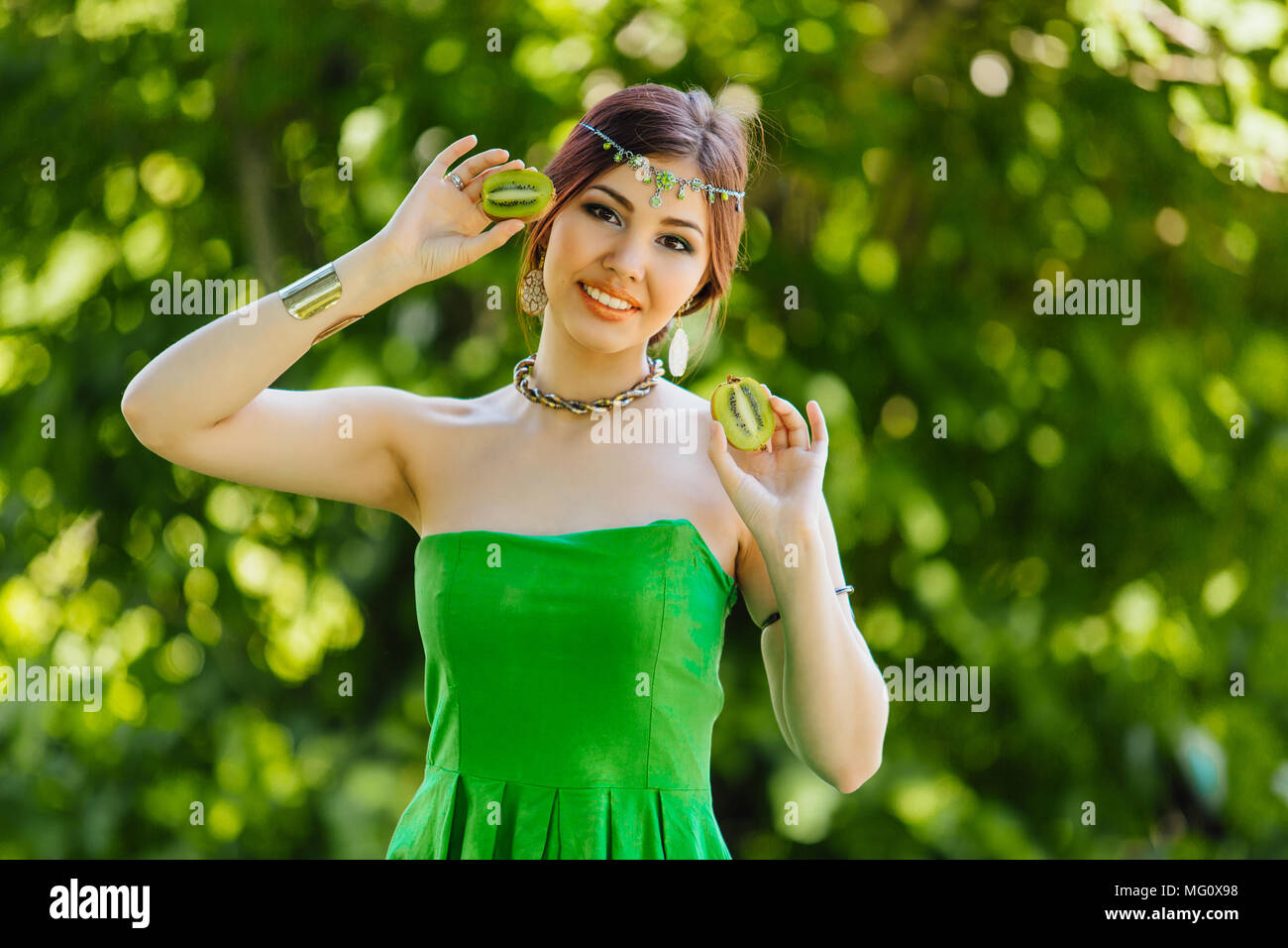 Portrait of a beautiful young asian woman holding two halves of kiwi ...