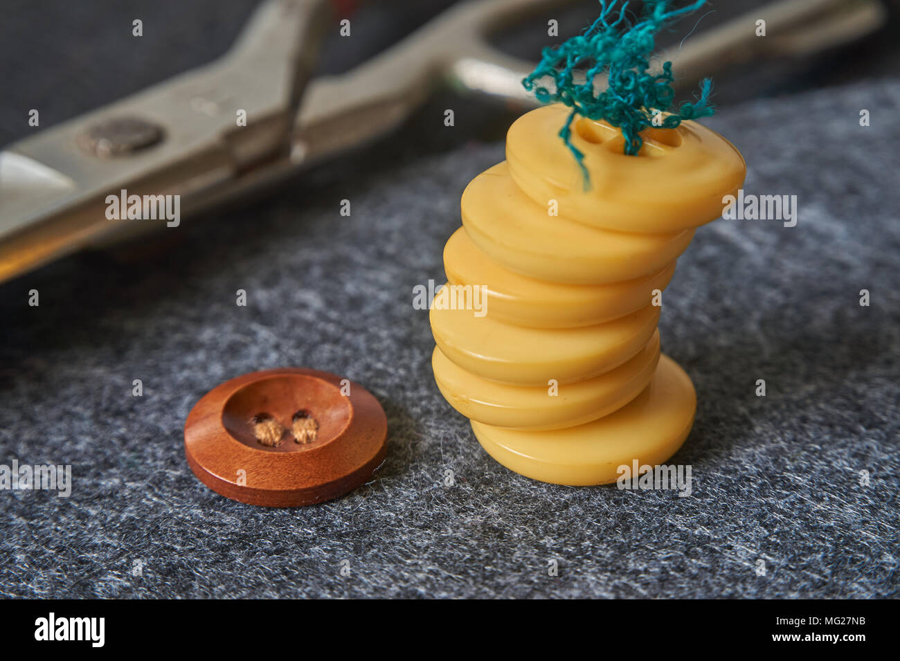 Sewing buttons, thread, scissors on needle punched nonwoven fabric background. Macro view, shallow depth of field. Stock Photo