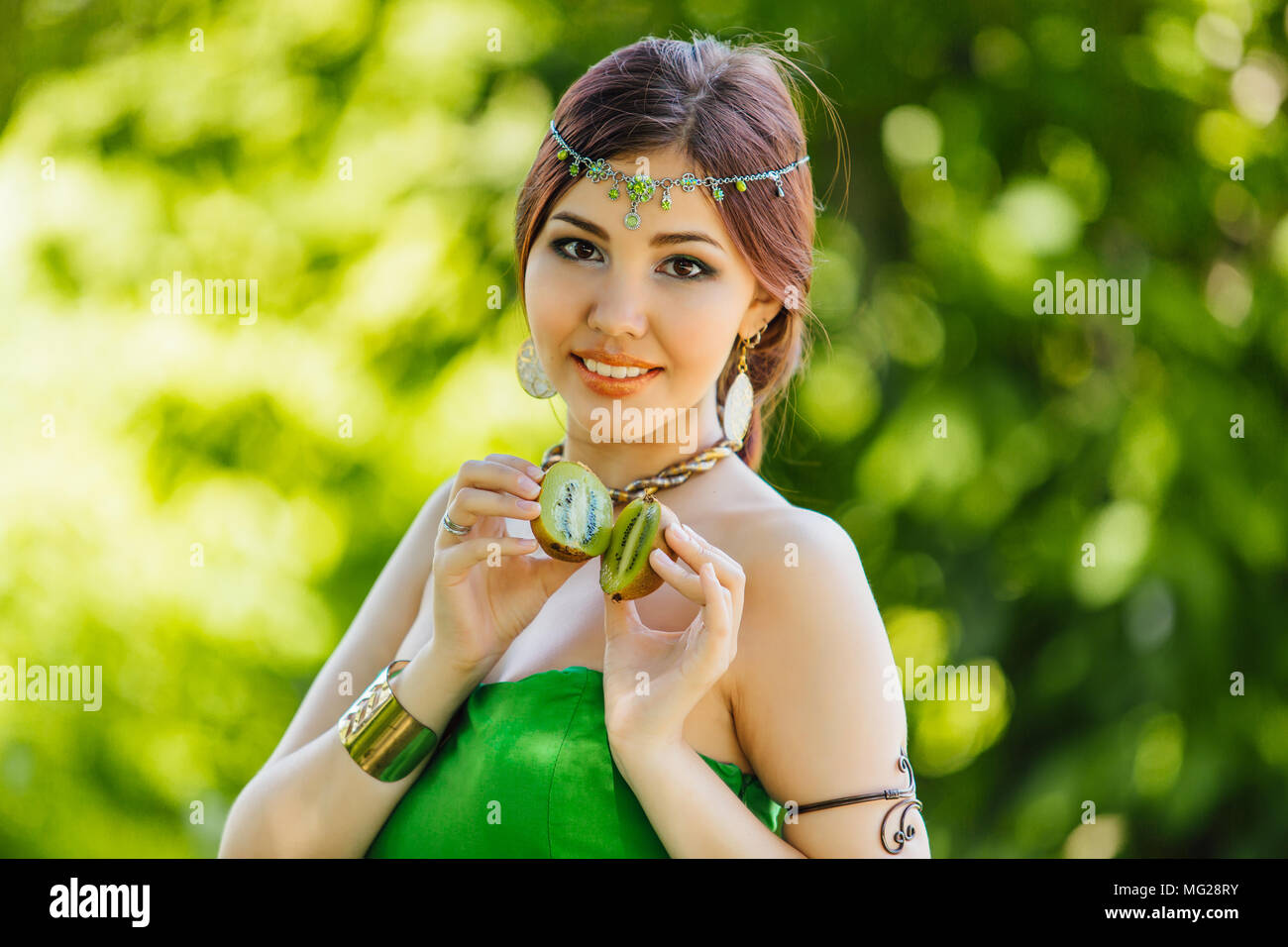 Portrait of a beautiful young asian woman holding two halves of kiwi ...