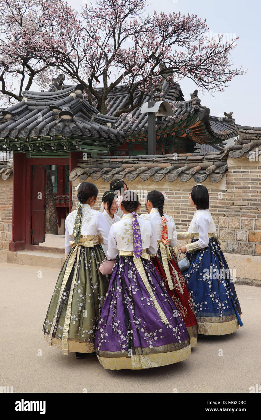 Group of six Korean teenage girls in colorful fullskirted traditional hanbok dress gather near a blooming cherry tree at Changdeokgung Palace in Seoul Stock Photo