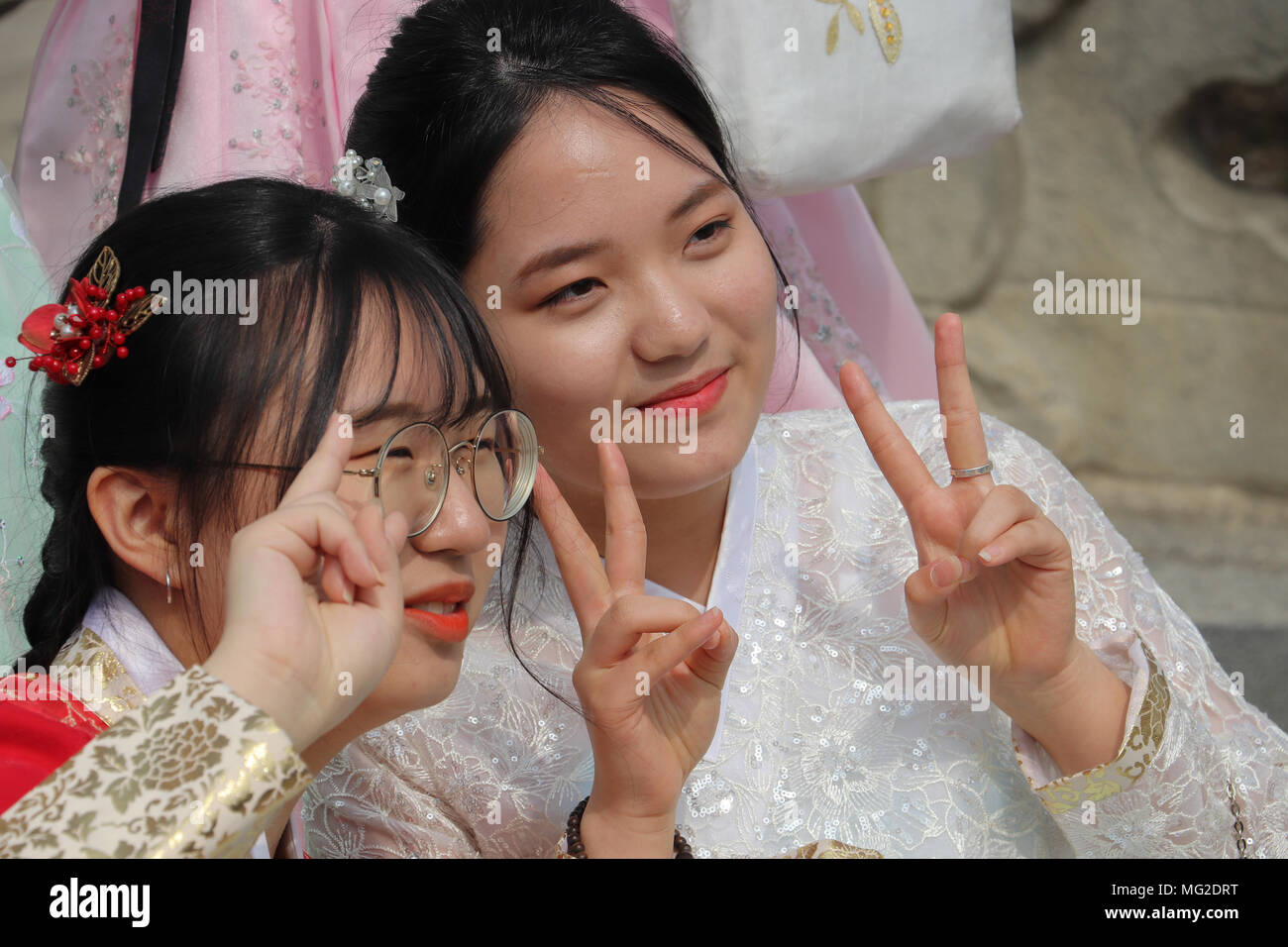 Korean teen girls flash a 'V'(Victory) sign, as they pose for photos, dressed in traditional hanbok fashion in Seoul, South Korea, on a school outing. Stock Photo