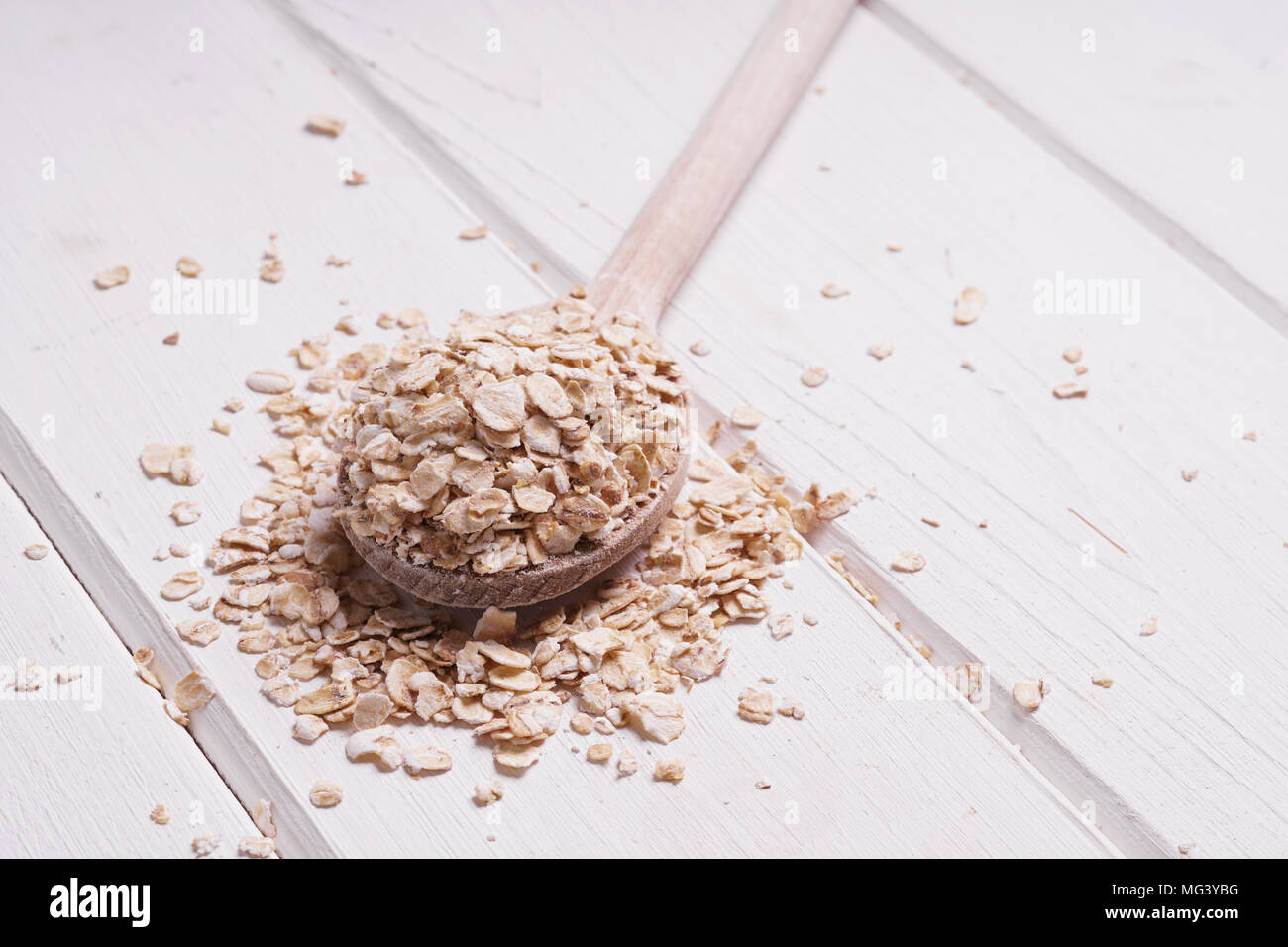 heaped rolled oats oatmeal oat flakes on wooden spoon on rustic white wooden table Stock Photo