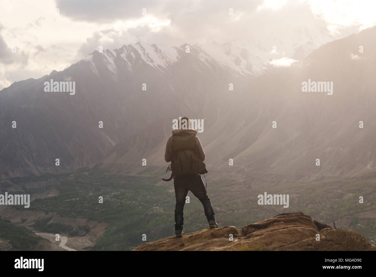 Traveller with backpack standing on mountain peak, enjoying beautiful sunset and valley view. Travel lifestyle and achievement success concept Stock Photo