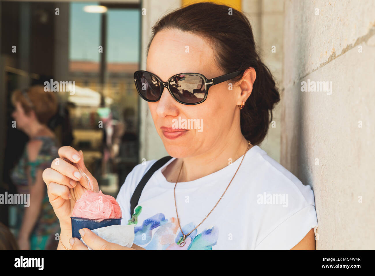 Young adult European woman eats pink ice cream, close-up outdoor portrait Stock Photo