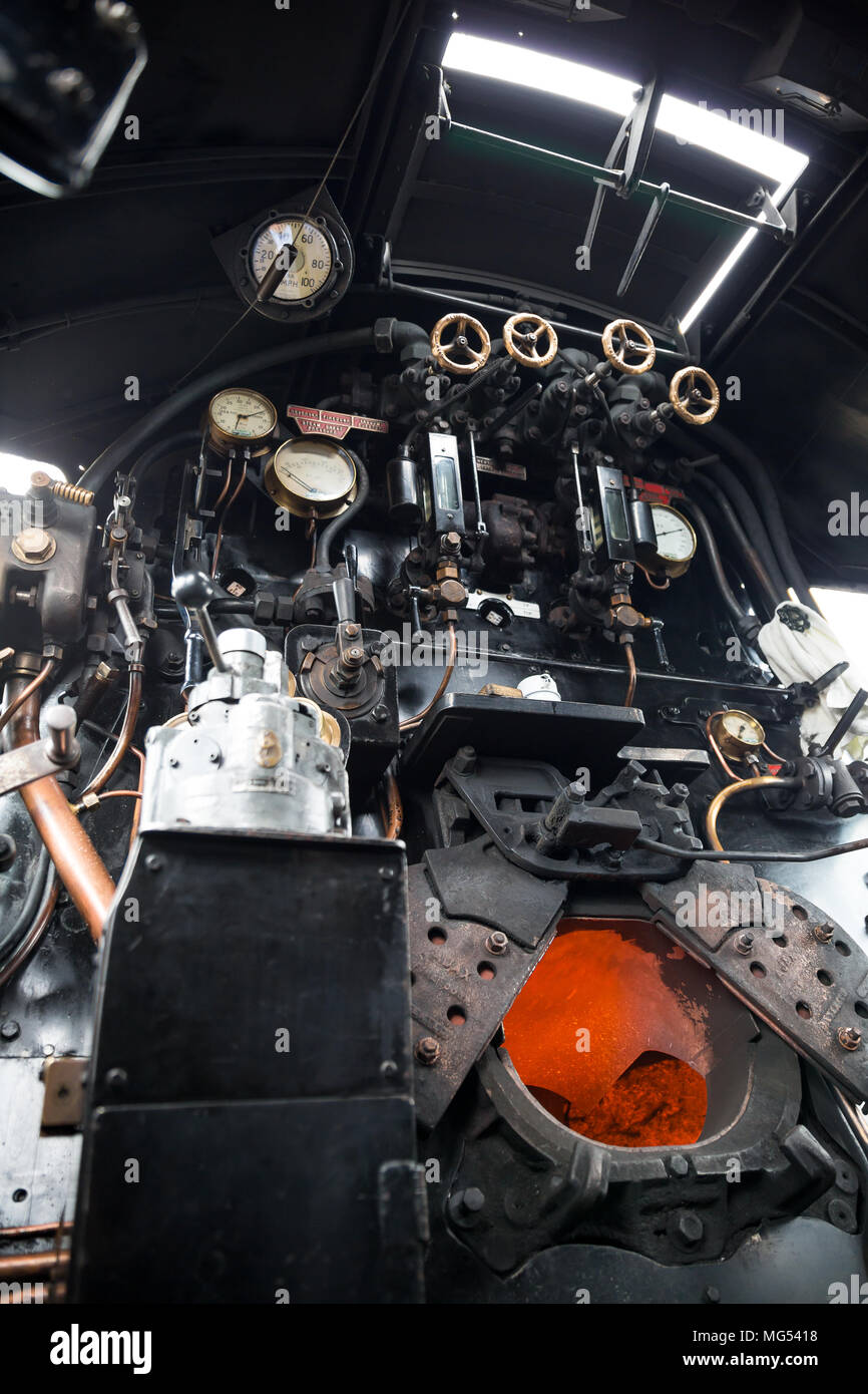 Low angle view inside steam locomotive cab of Taw Valley, fire doors open showing orange heat glow of burning fuel in the firebox. Stock Photo