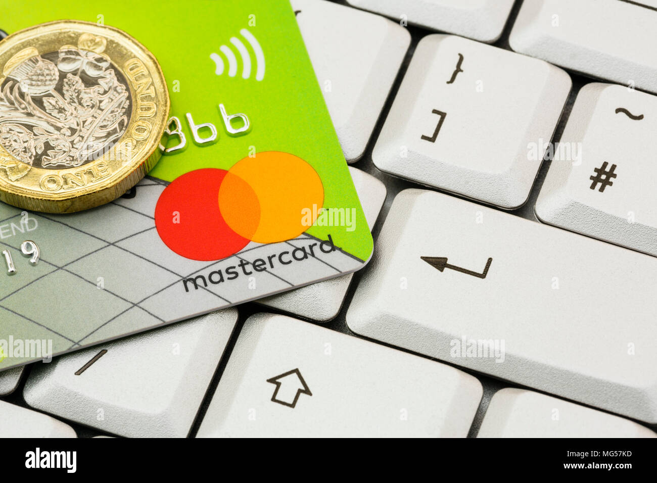 Lloyds bank Mastercard contactless credit card and one pound coin on a computer keyboard with enter key. Online internet shopping concept. England UK Stock Photo