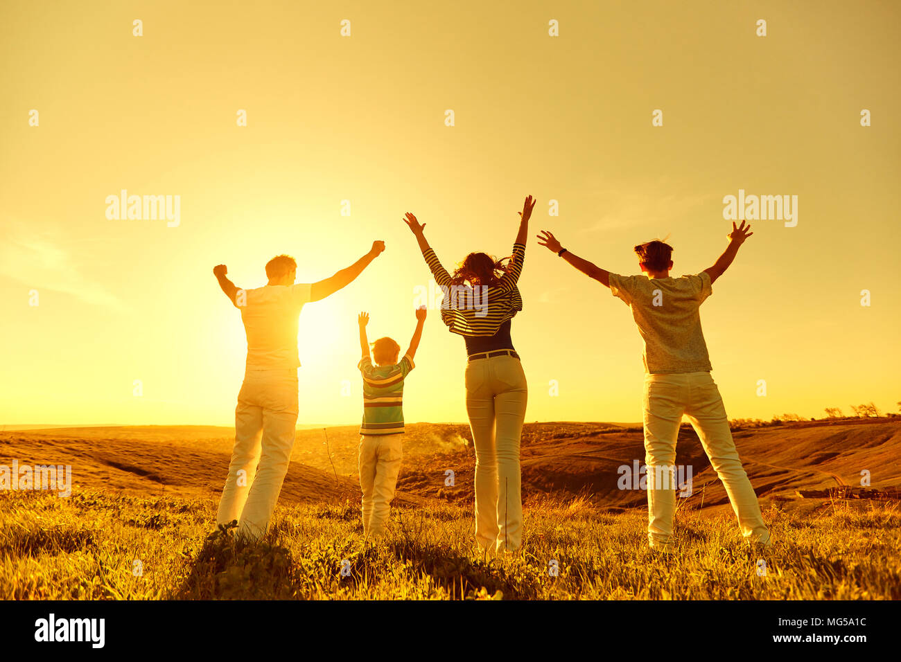 Happy family with raised hands on nature at sunset. Stock Photo