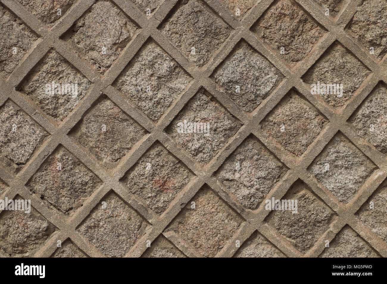Patterned stone wall with squares set diagonally like a lattice. This wall is sand colored, would make good background. Slight shadows, daylight. Stock Photo