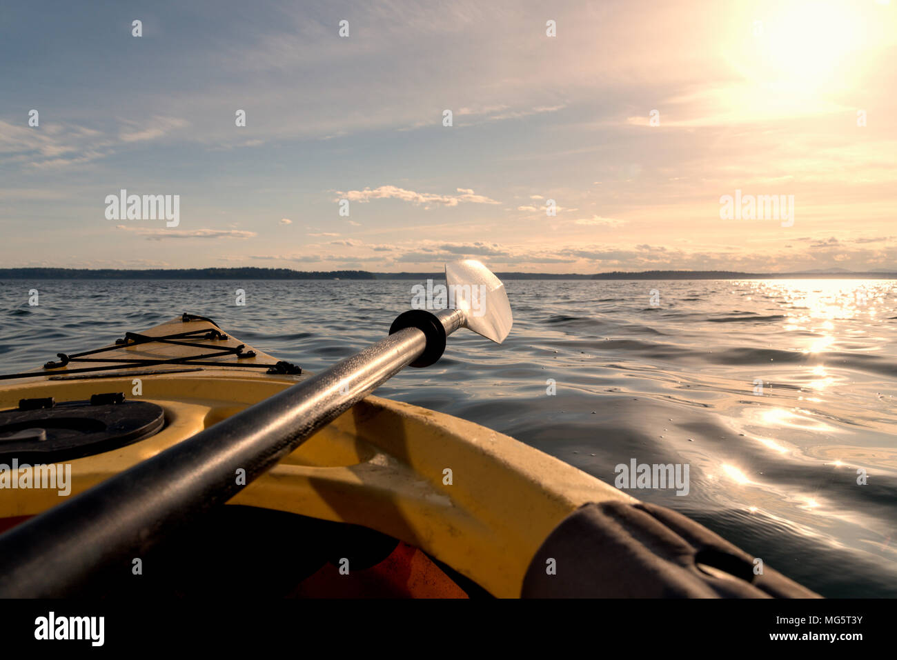 Point of view kayak at dusk on beautiful Puget Sound near Seattle, paddle resting on side of boat pointing at sun. Stock Photo