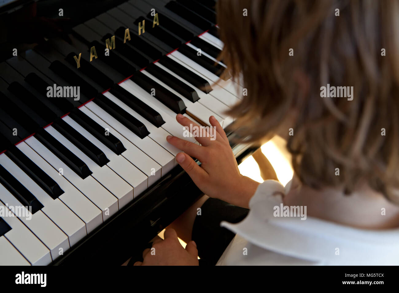 A young boy, aged six, practises playing the piano Stock Photo