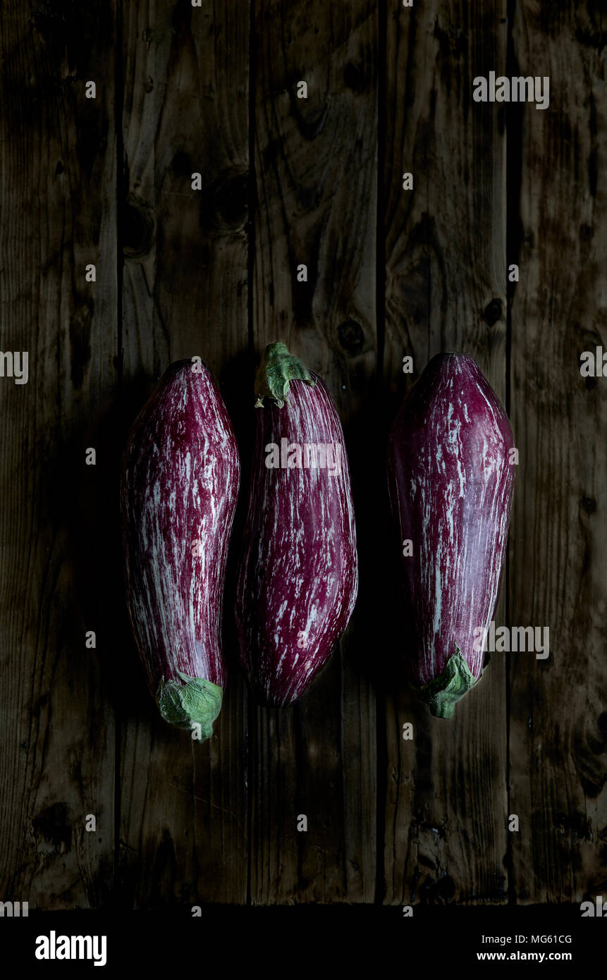 Three Nubia eggplants over a rustic wooden table in a darkness ambient. Stock Photo