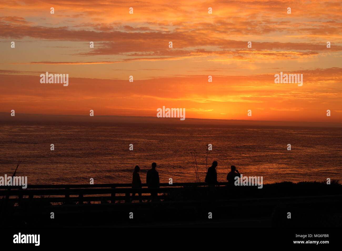 An evening stroll on the boardwalk among a brilliant California sunset over the mighty Pacific Ocean. Stock Photo