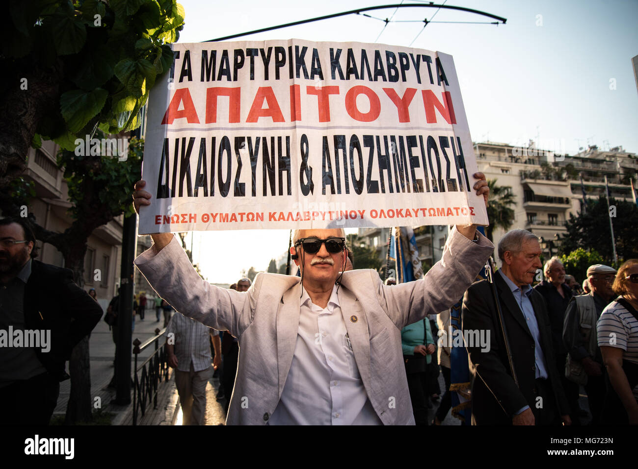 Athens, Greece. 27th Apr, 2018. A protester seen holding a placard during the demonstration.First gathering at the Unknown Soldier's Monument, the march has been made until the German Embassy to protest for compensation of the World War II from Germany as several massacre perpetuated by German soldiers back in 1943 were committed. Credit: Vangelis Evangeliou/SOPA Images/ZUMA Wire/Alamy Live News Stock Photo