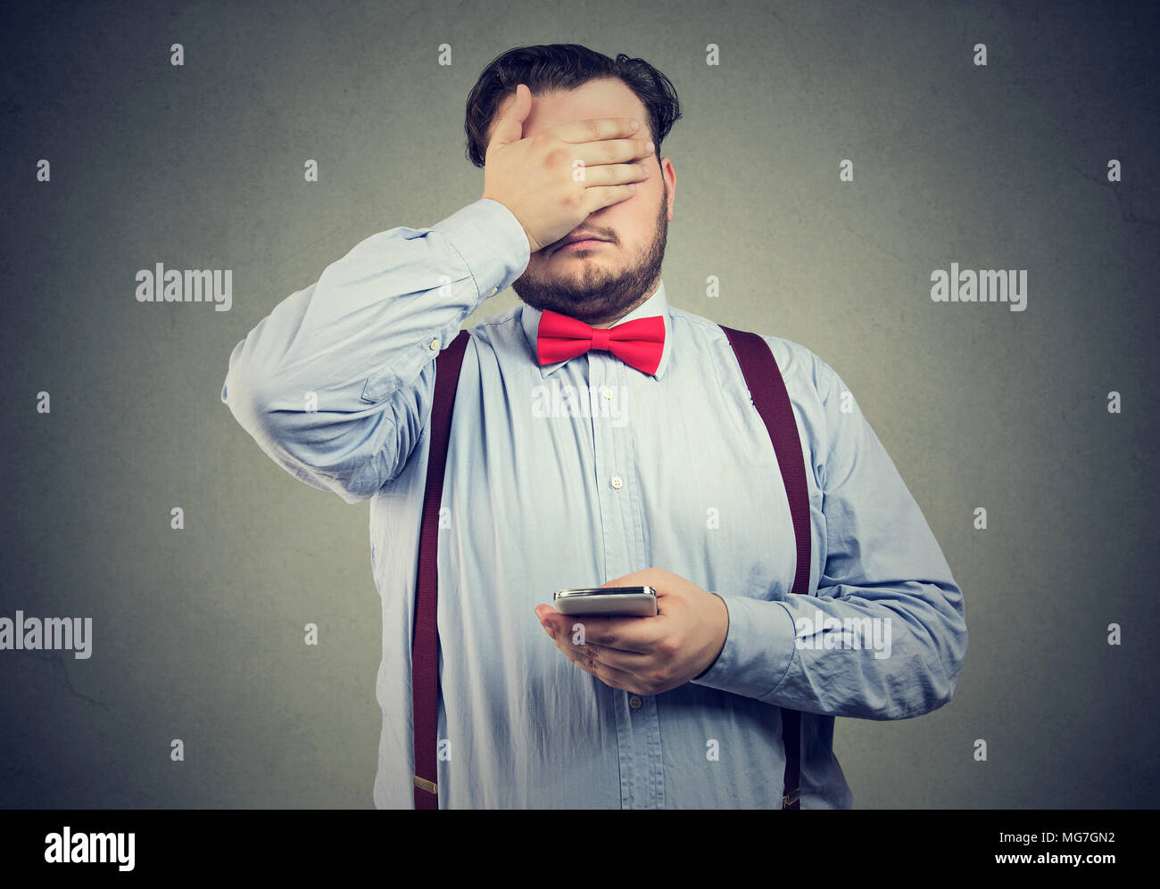 Sad regretful young man with mobile phone covering with hand his face Stock Photo