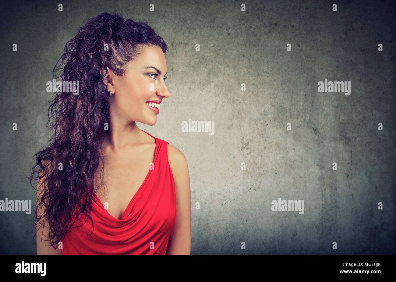 Portrait of a young smiling woman in red dress isolated on gray wall ...