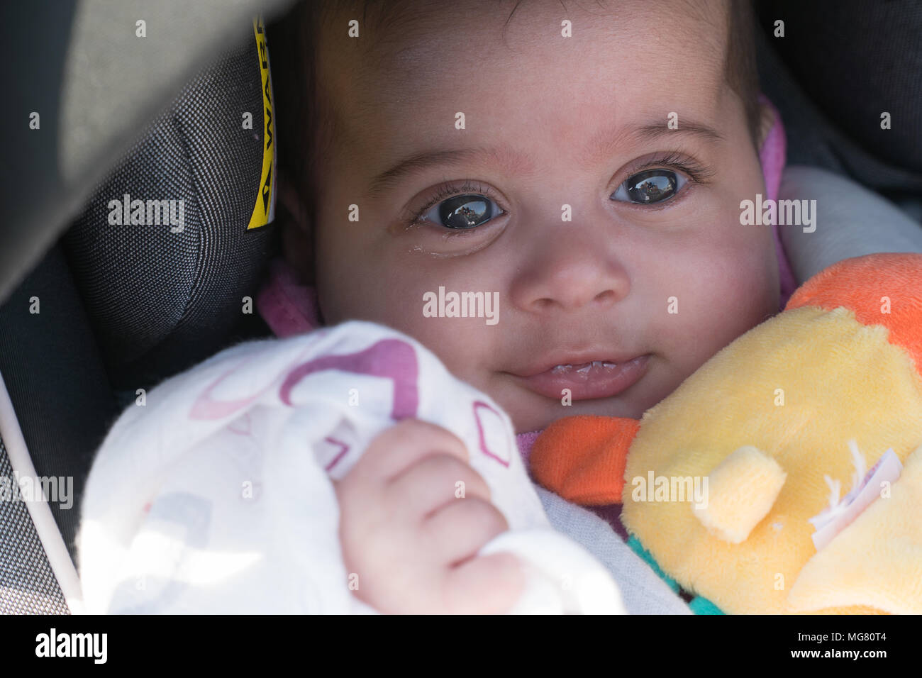 Cute young happy infant baby in car seat smiling. Watery tear eyes and