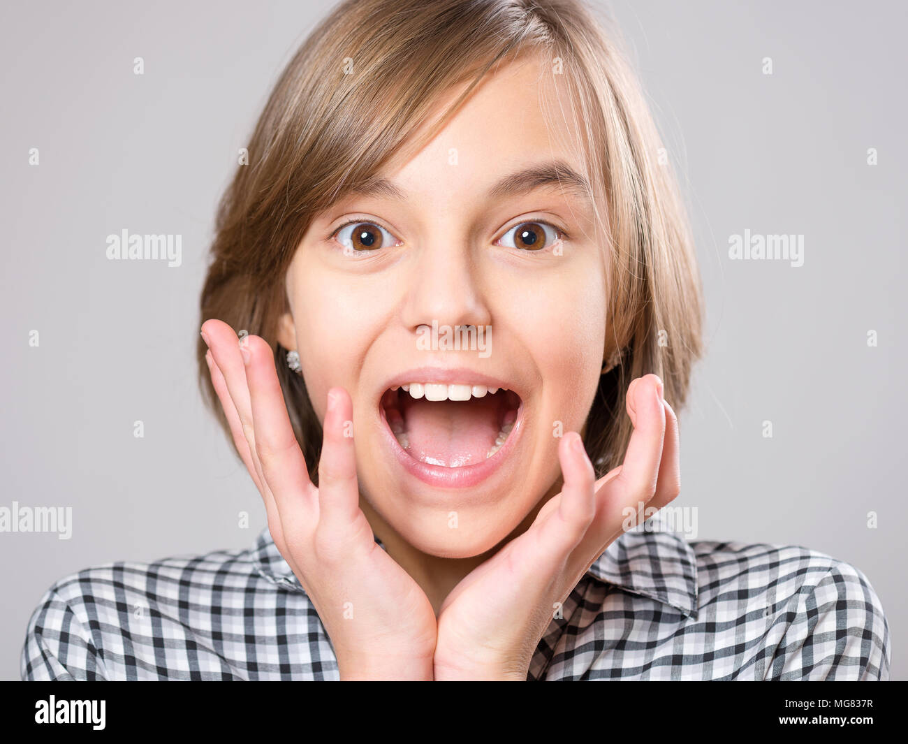 Close-up emotional portrait of excited little girl. Funny cute surprised child 10 year old with mouth open in amazement. Shocked teenager, on gray bac Stock Photo