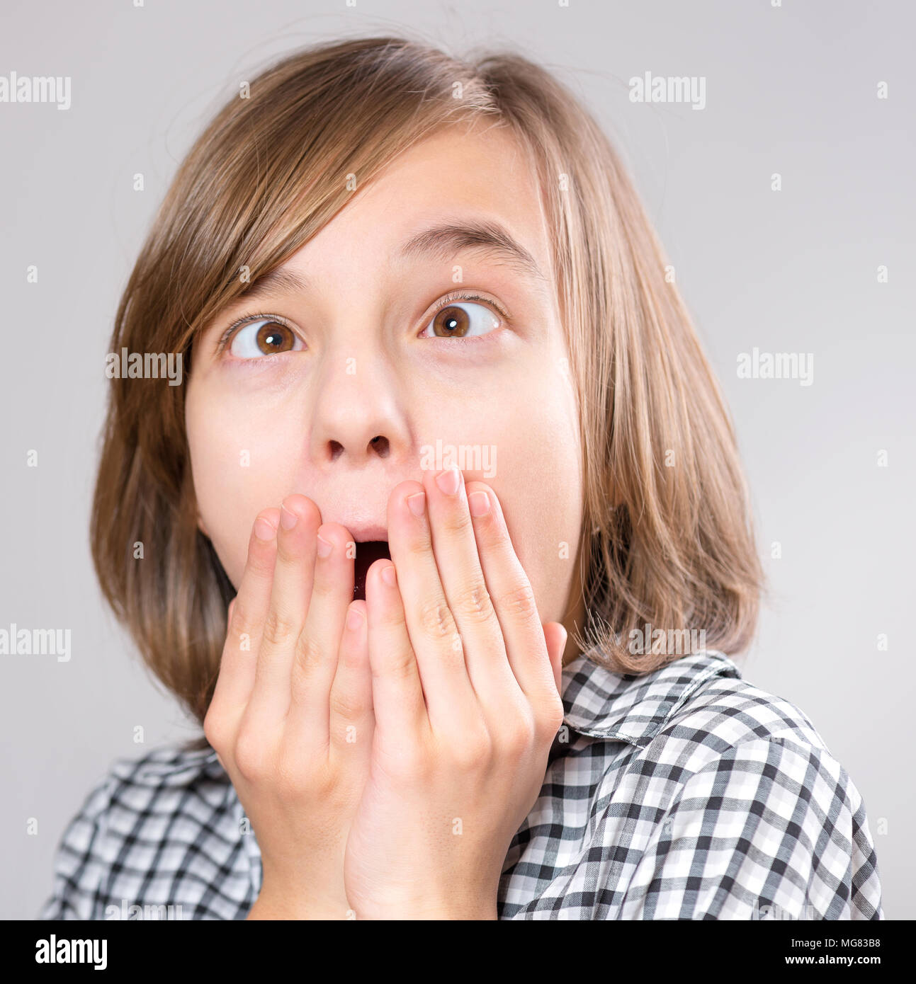 Silly girl making grimace - funny face. Child on gray background. Emotional portrait of caucasian teenager looking at camera. Stock Photo