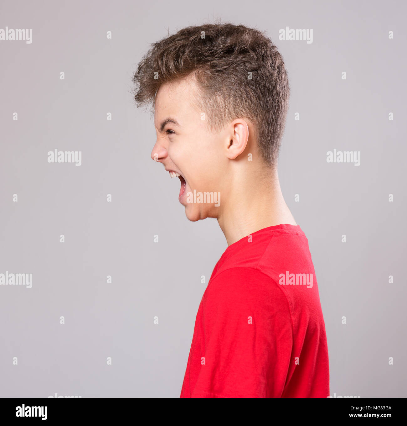 Emotional portrait of profile irritated shouting teen boy. Furious teenager screaming and looking away. Handsome outraged child shouting out loud on g Stock Photo