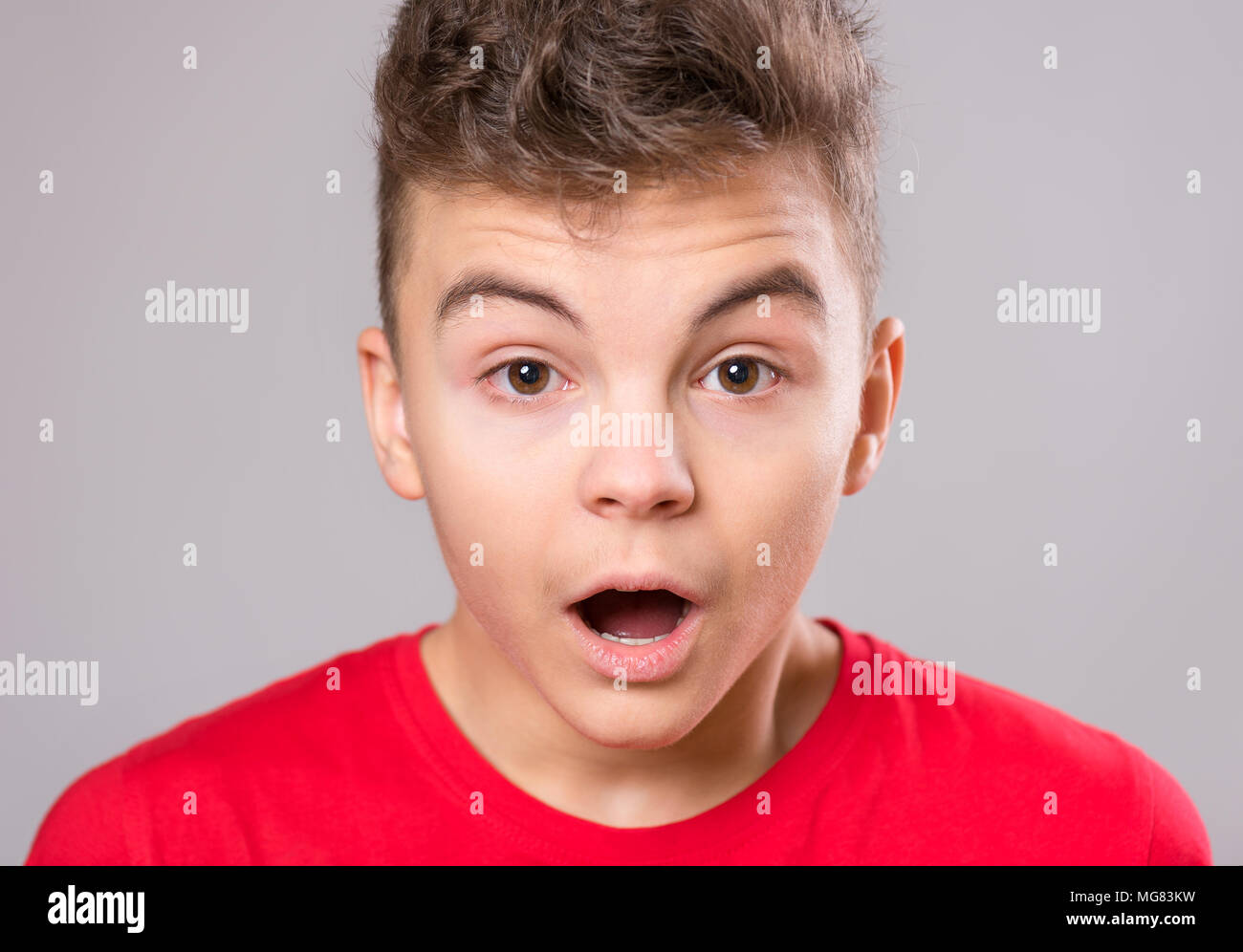 Emotional portrait of caucasian teen boy - surprised teenager looking at camera. Handsome child, on gray background. Stock Photo