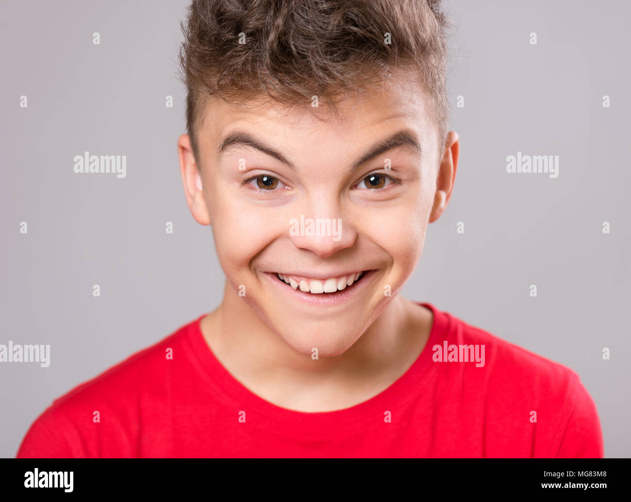 Silly teen boy making grimace - funny face. Child on gray background. Emotional portrait of caucasian teenager looking at camera. Stock Photo
