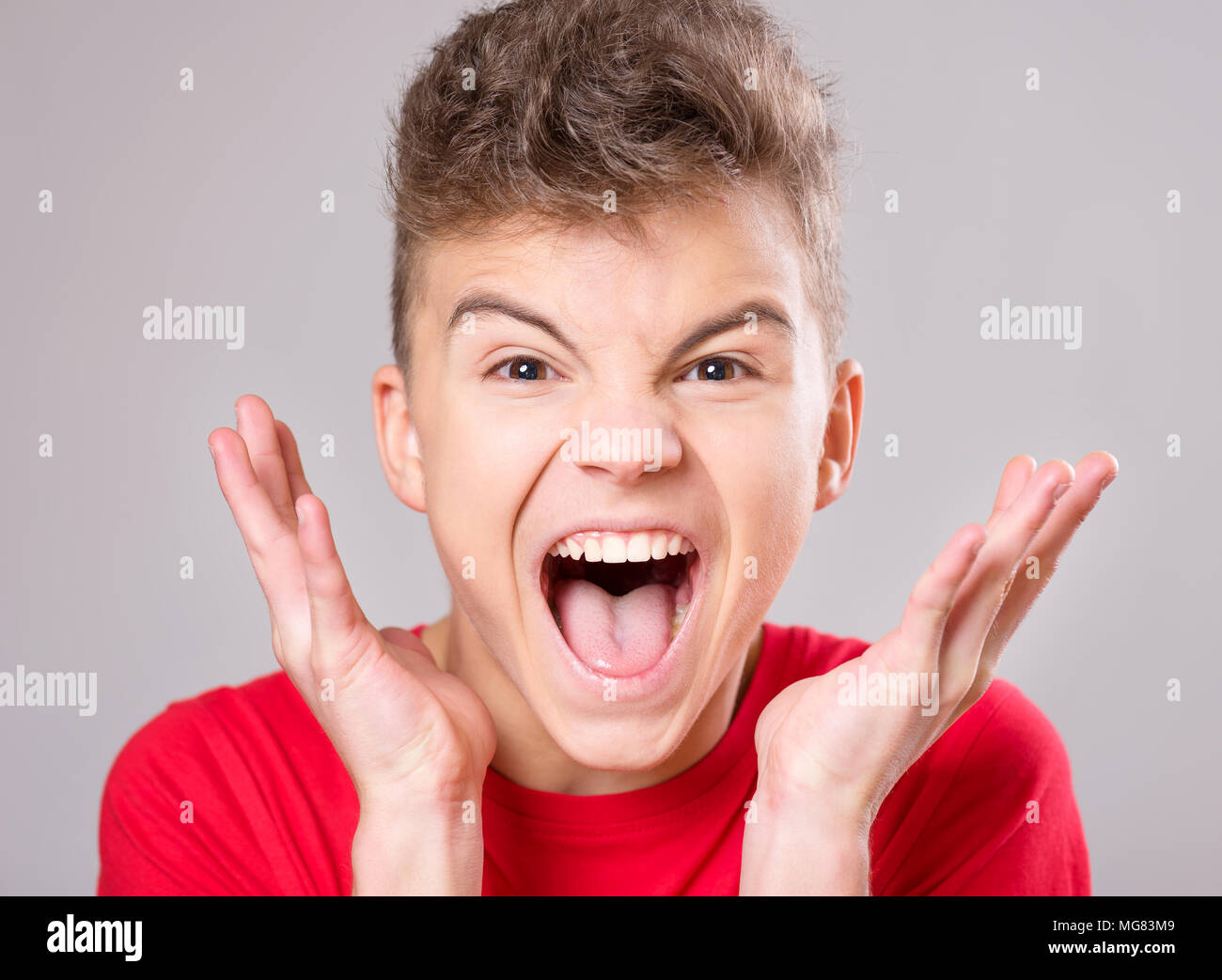 Emotional portrait of irritated shouting teen boy. Furious teenager screaming and looking with anger at camera. Handsome outraged child shouting out l Stock Photo