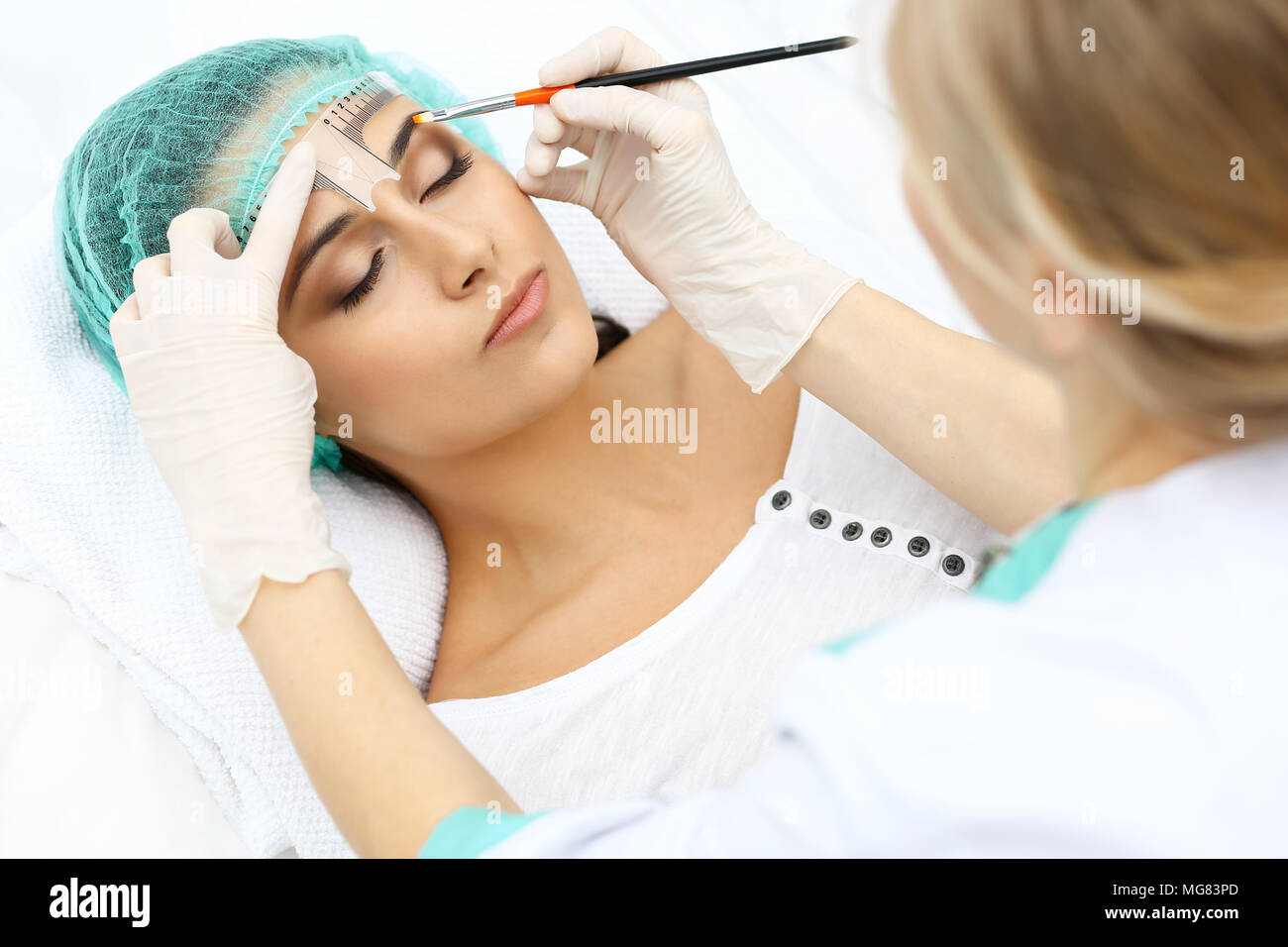 Professional beautician is going to correct eyebrow line at woman face ...