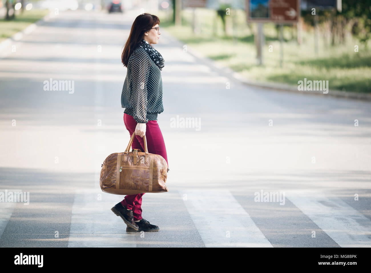 The woman with brown leather bag crosses a pedestrian crossing Stock Photo