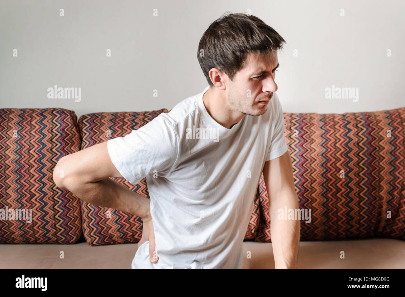 A Man Suffering From Back Pain At Home On The Couch Concept Of