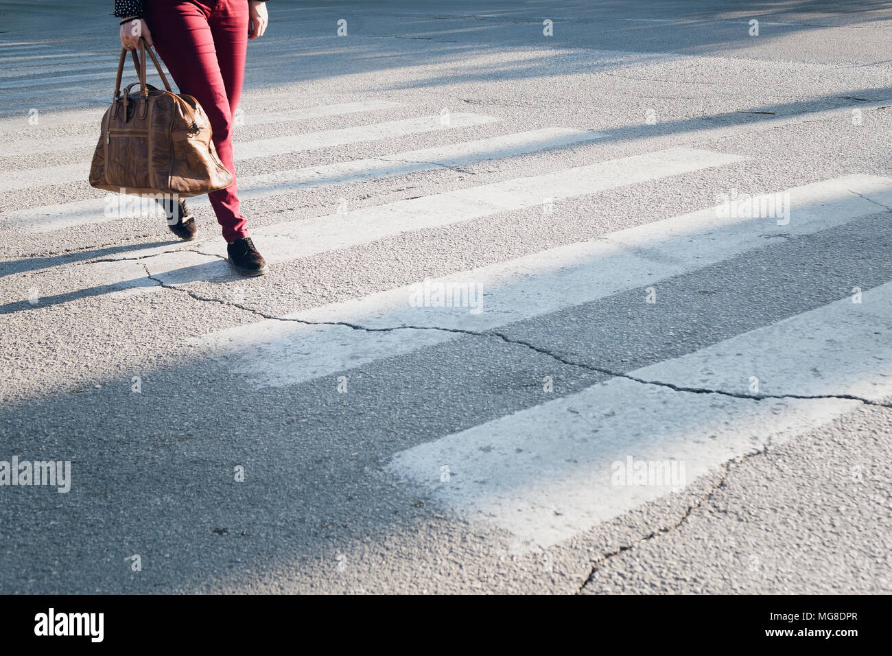 The woman with brown leather bag crosses a pedestrian crossing Stock Photo