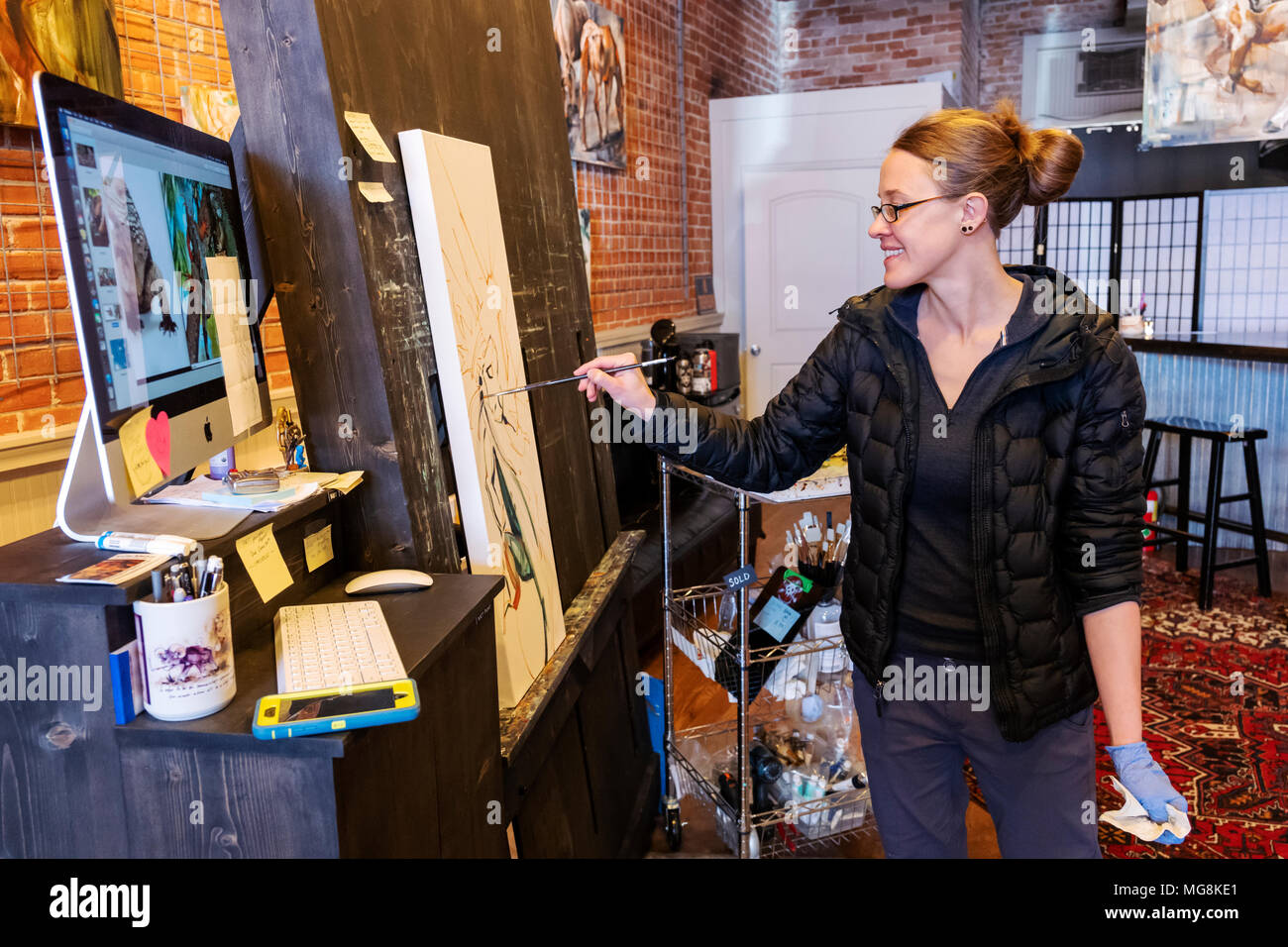 Fine artist Katie Maher referencing a computer image while creating an oil painting in her gallery; Salida; Colorado; USA Stock Photo