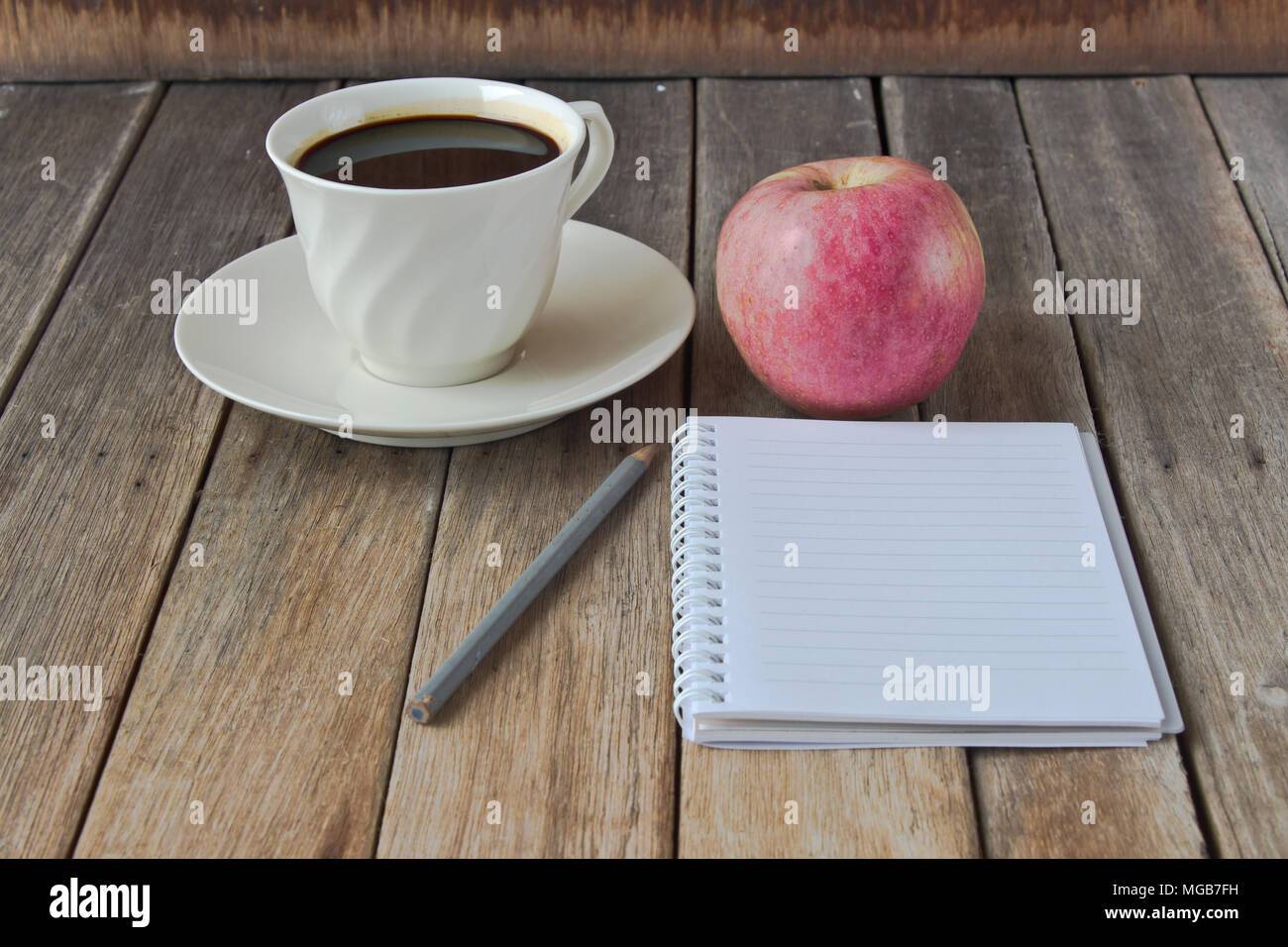 Notebook with pencil, coffee cup and red apple on wood table Stock Photo