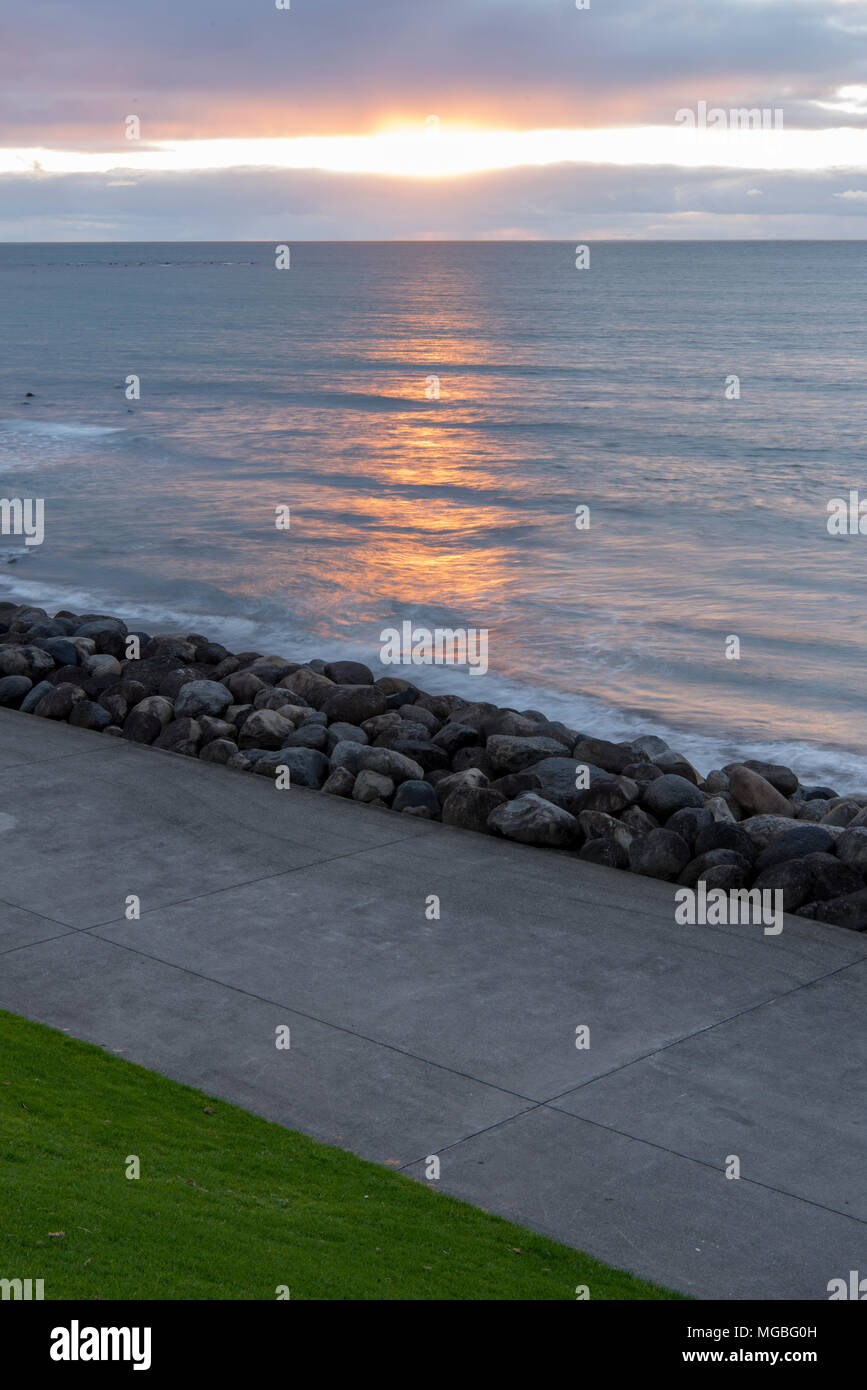 Sea Setting Example Sun setting at sea with sea wall pavement and grass Stock Photo - Alamy