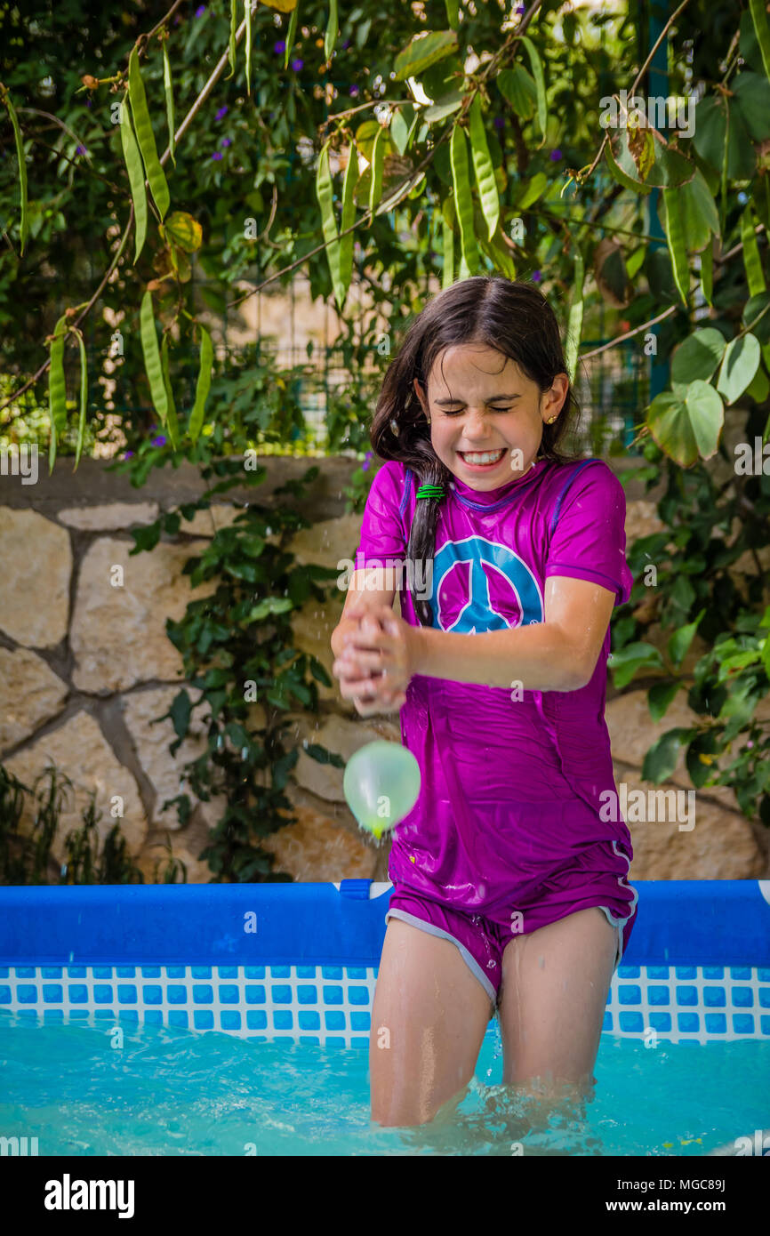 Young girl in a bathing suit try to catch water balloon in the pool in