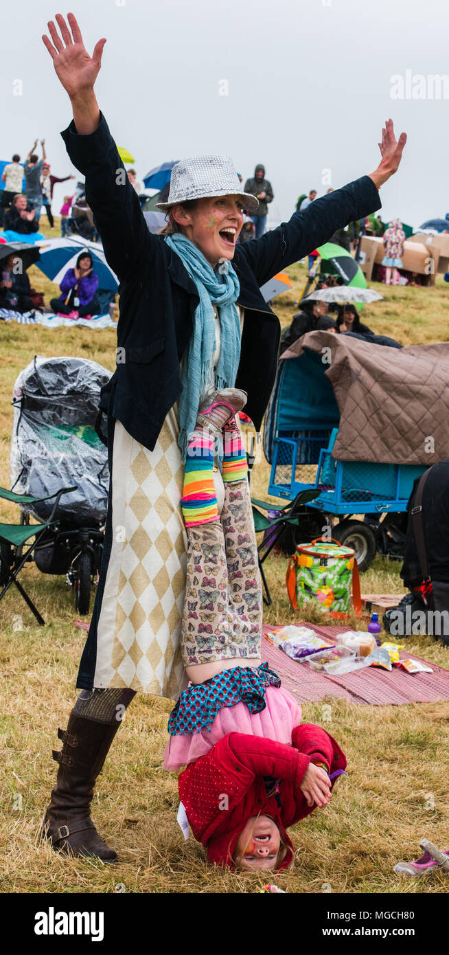 Woman singing, outstretched arms while young girl stands on her head in front of her, Deer Shed Festival,Baldersby Park, North Yorkshire, July 2015 Stock Photo