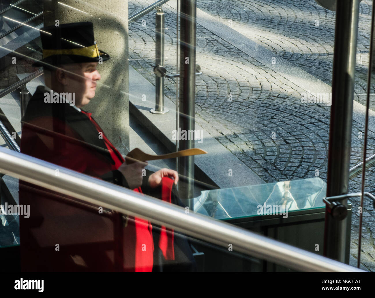 Doorman with top hat putting coat on coat hanger, seen through glass window Stock Photo