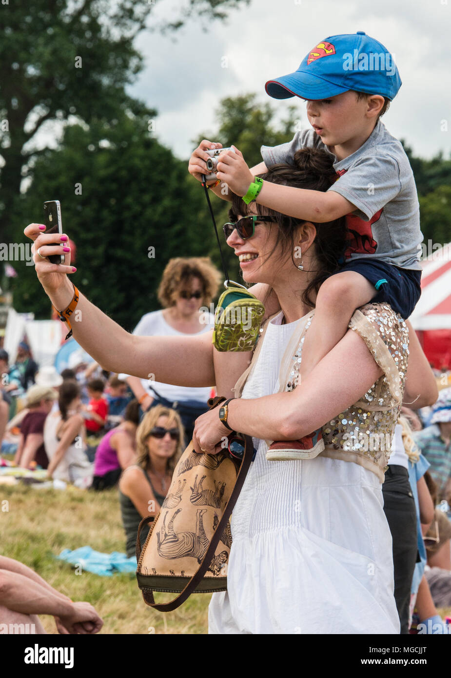Mother and son at festival, mother taking selfie of son sitting on her shoulders, while her son takes a photo too, using camera Stock Photo