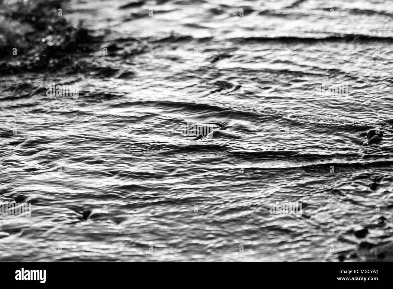 A close view of water on a lake shore at sunset, with details of sands and little round stones Stock Photo