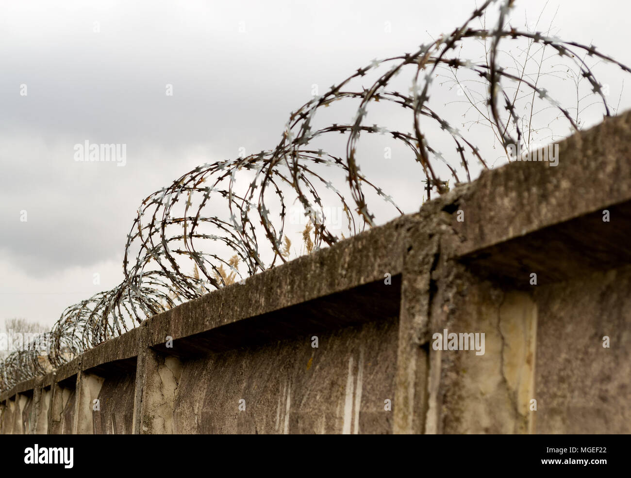barbed wire fence and stone wall at the cloud sky Stock Photo