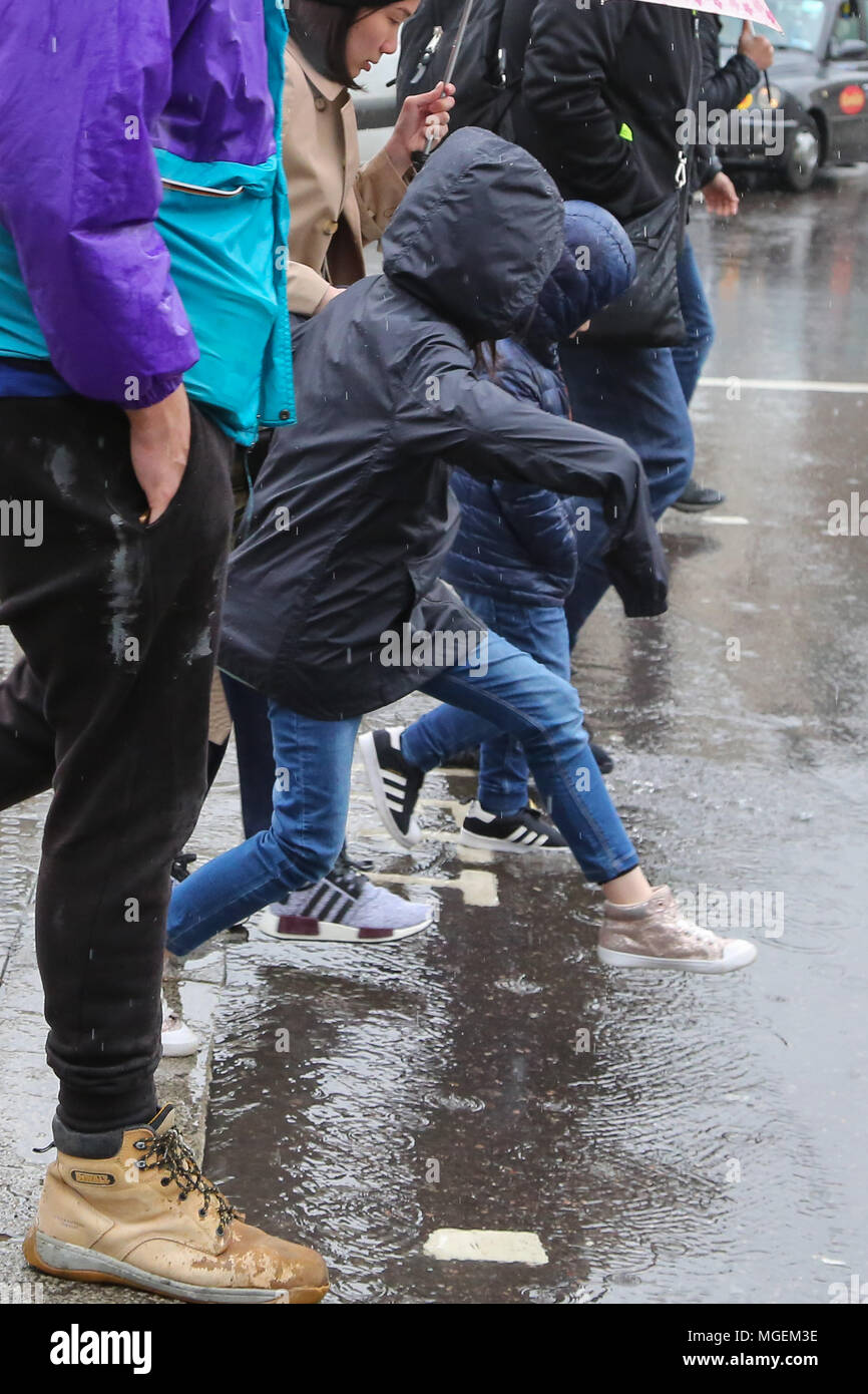 Tourists With Umbrellas And Wearing Rain Ponchos In The Rain Avoiding Puddle Of Rainwater Near Trafalgar