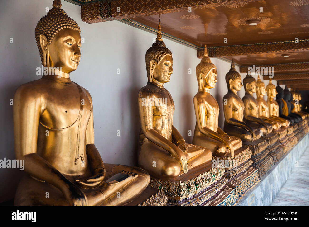 Gold statues of Buddha placed in a row under an ornamental ceiling, are located in the temple of Wat Pho in Bangkok where there is also a large statue Stock Photo