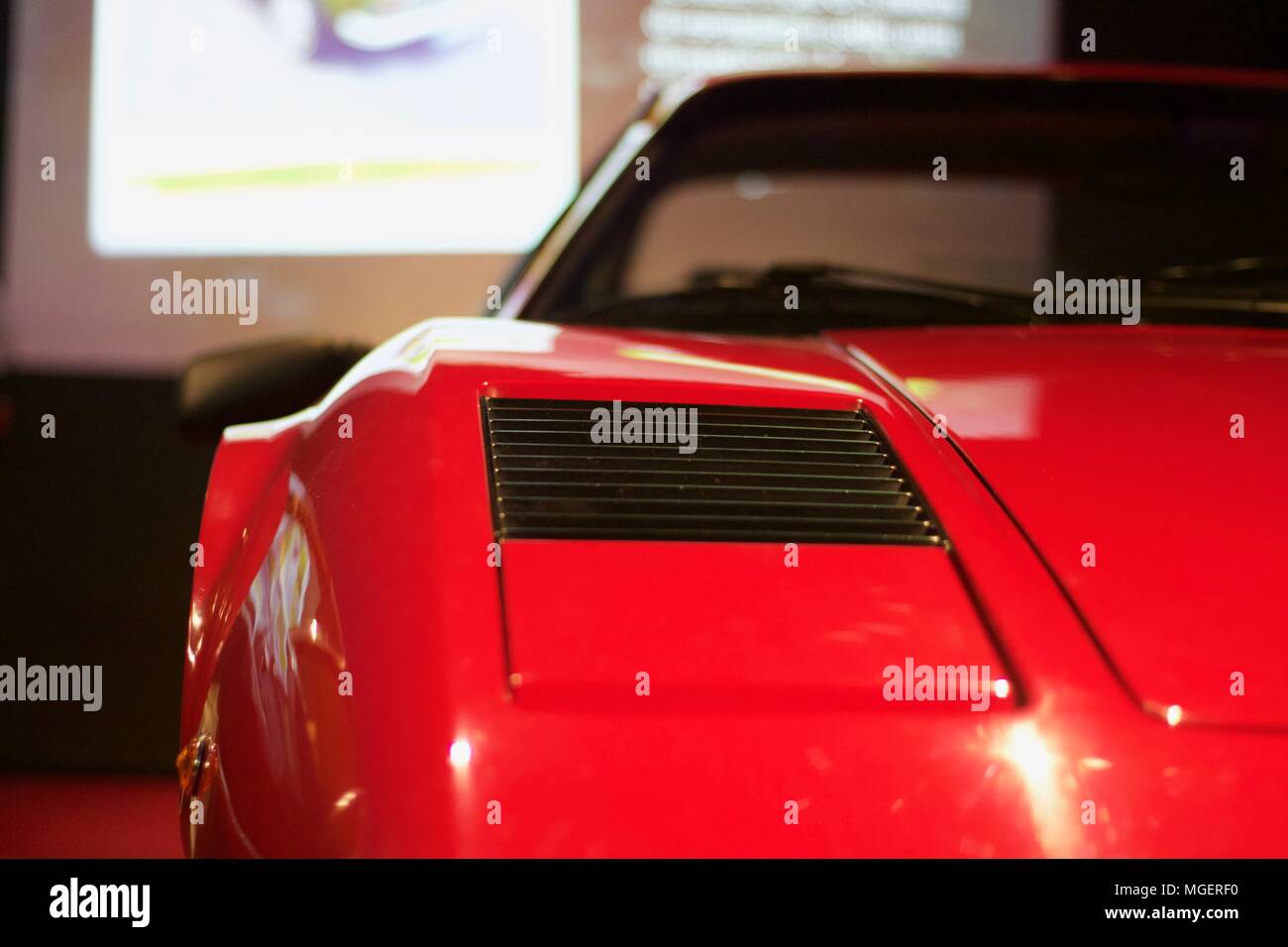 Red snout of a Ferrari Testarossa that protrudes from the wall, with the well-lit Ferrari logo and the reflection of the light on the bonnet Stock Photo